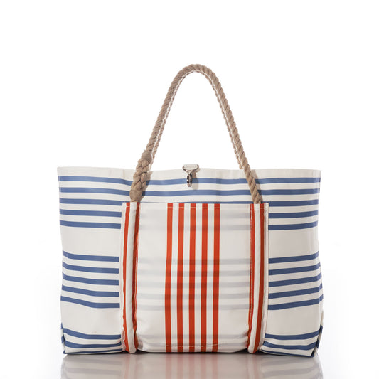 The Picnic Stripe Pier Tote by Sea Bags is a white nautical tote bag featuring horizontal blue stripes, vertical orange stripes on the front pocket, and two rope handles. Crafted from recycled sail cloth for weatherproof durability and style, it is photographed against a white background. by Sea Bags