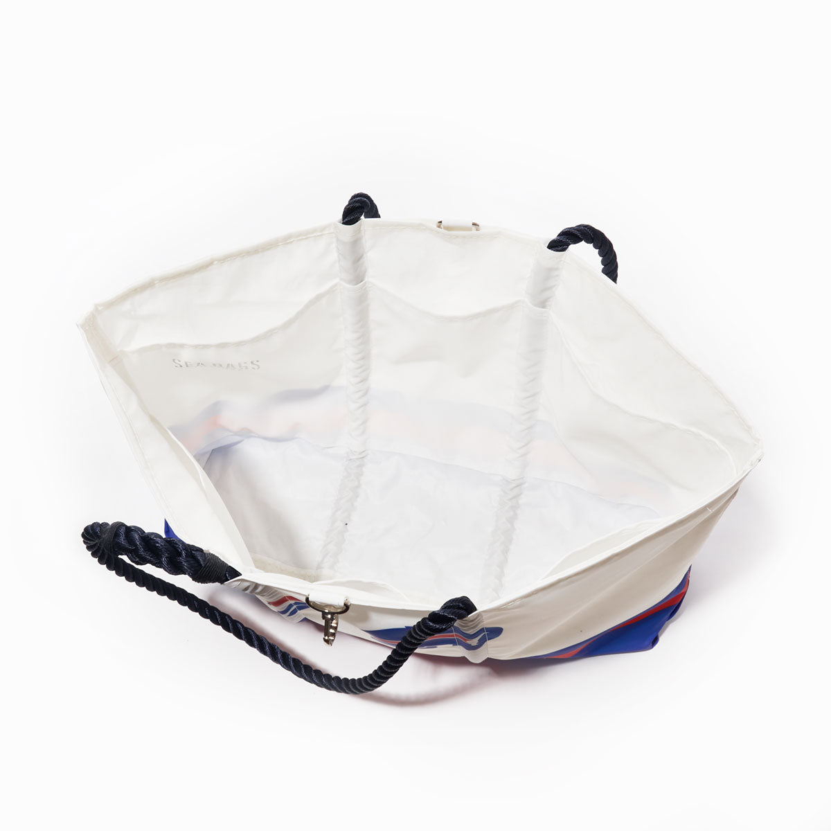 The Buffalo Bills Tailgate Tote by Sea Bags, made from recycled sail cloth and featuring a blue and red striped exterior with black rope handles, is shown open and empty from above on a white background. by Sea Bags