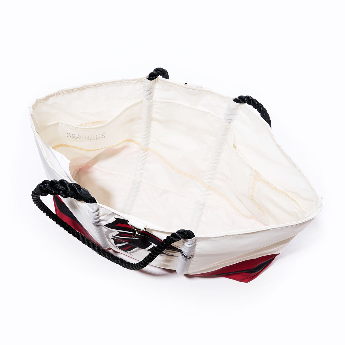 Open white Atlanta Falcons Tailgate Tote by Sea Bags featuring black rope handles, red and black exterior detailing, and a visible Sea Bags label on the inner lining against a white background—crafted from recycled sail cloth for a durable and eco-friendly NFL logo bag. by Sea Bags