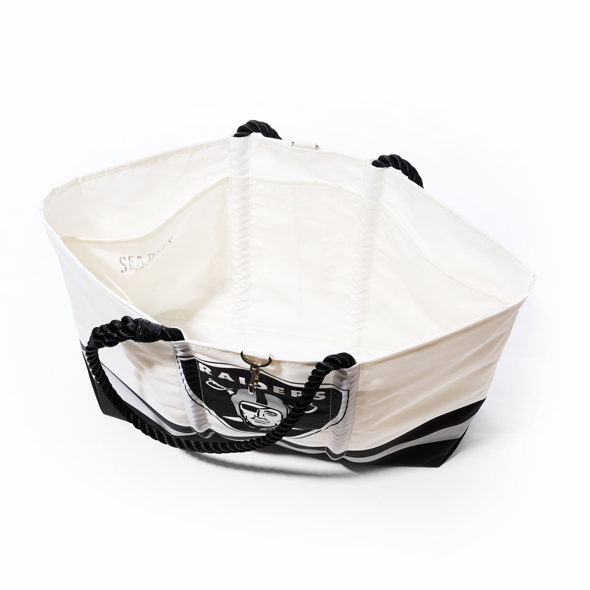 The Sea Bags Las Vegas Raiders Tailgate Tote is a spacious white tote bag crafted from recycled sail cloth, featuring sturdy black rope handles and a prominently displayed Raiders logo on the side. Photographed from above on a white background, this eco-friendly NFL tote is perfect for fans looking for durability and team spirit. by Sea Bags
