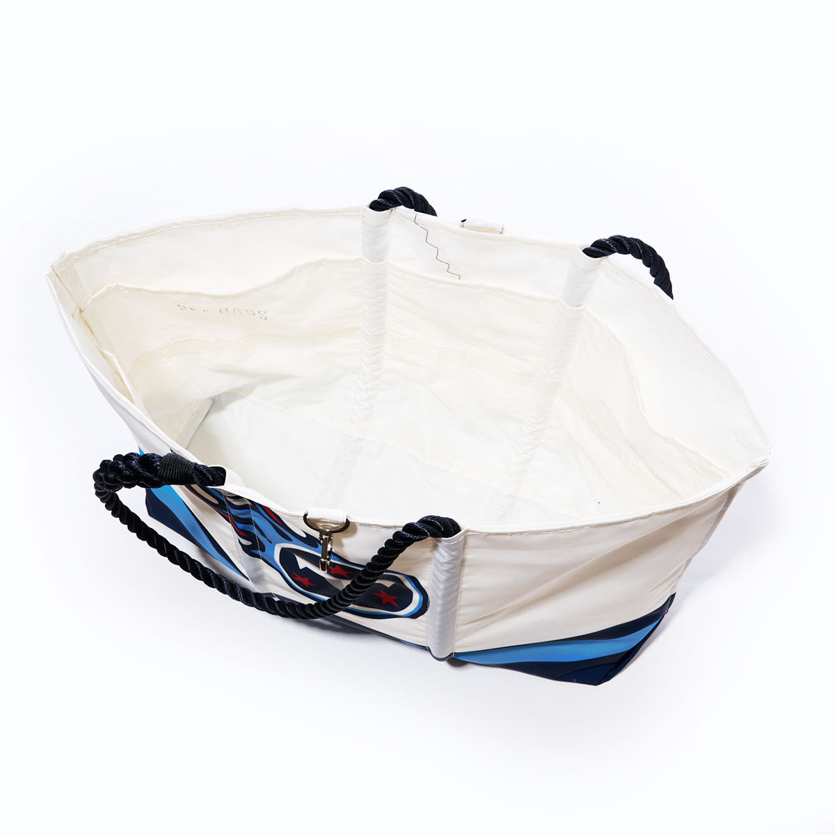 The Tennessee Titans Tailgate Tote by Sea Bags is a large white recycled sail cloth bag featuring navy rope handles and a bold blue, red, and black design on the side. Shown from above to highlight its spacious, empty interior, this tote is the perfect game day accessory. by Sea Bags
