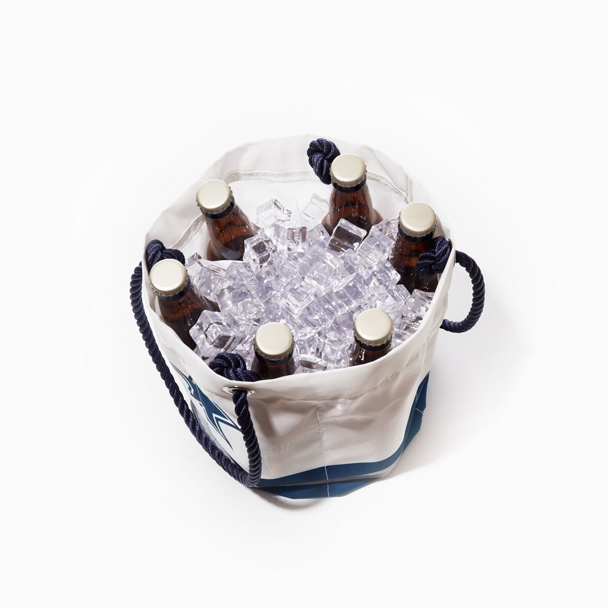 A white Dallas Cowboys Beverage Bucket by Sea Bags, featuring rope handles, holds six capped beer bottles nestled in ice cubes against a plain white background. Stylish and functional, this cooler is perfect for any gathering, blending convenience with team spirit. by Sea Bags
