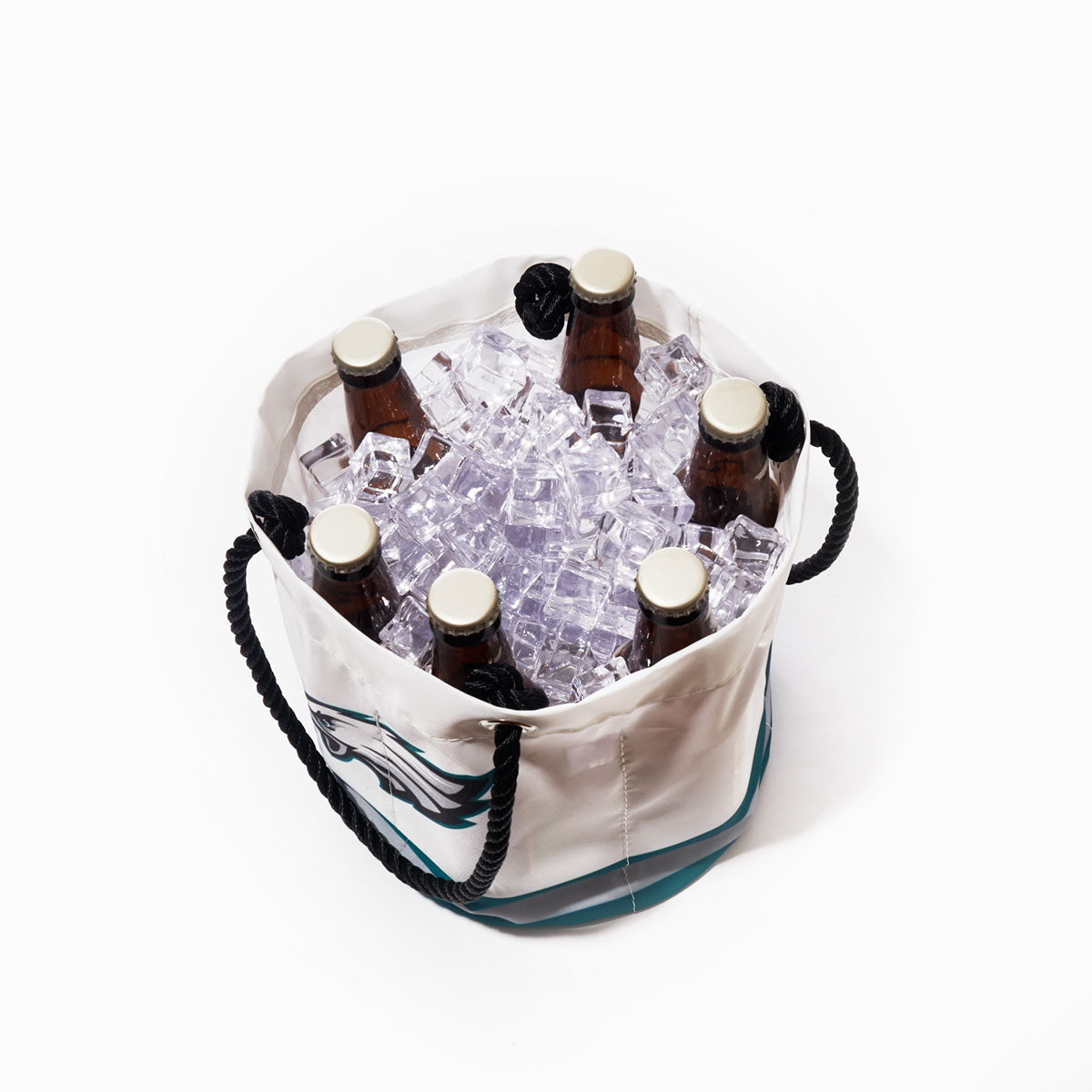 Six brown glass bottles with white caps are in the Sea Bags Philadelphia Eagles Beverage Bucket, which is crafted from recycled sail cloth and features black rope handles and a green Eagles design. The white bucket is filled with ice cubes and set against a plain white background. by Sea Bags