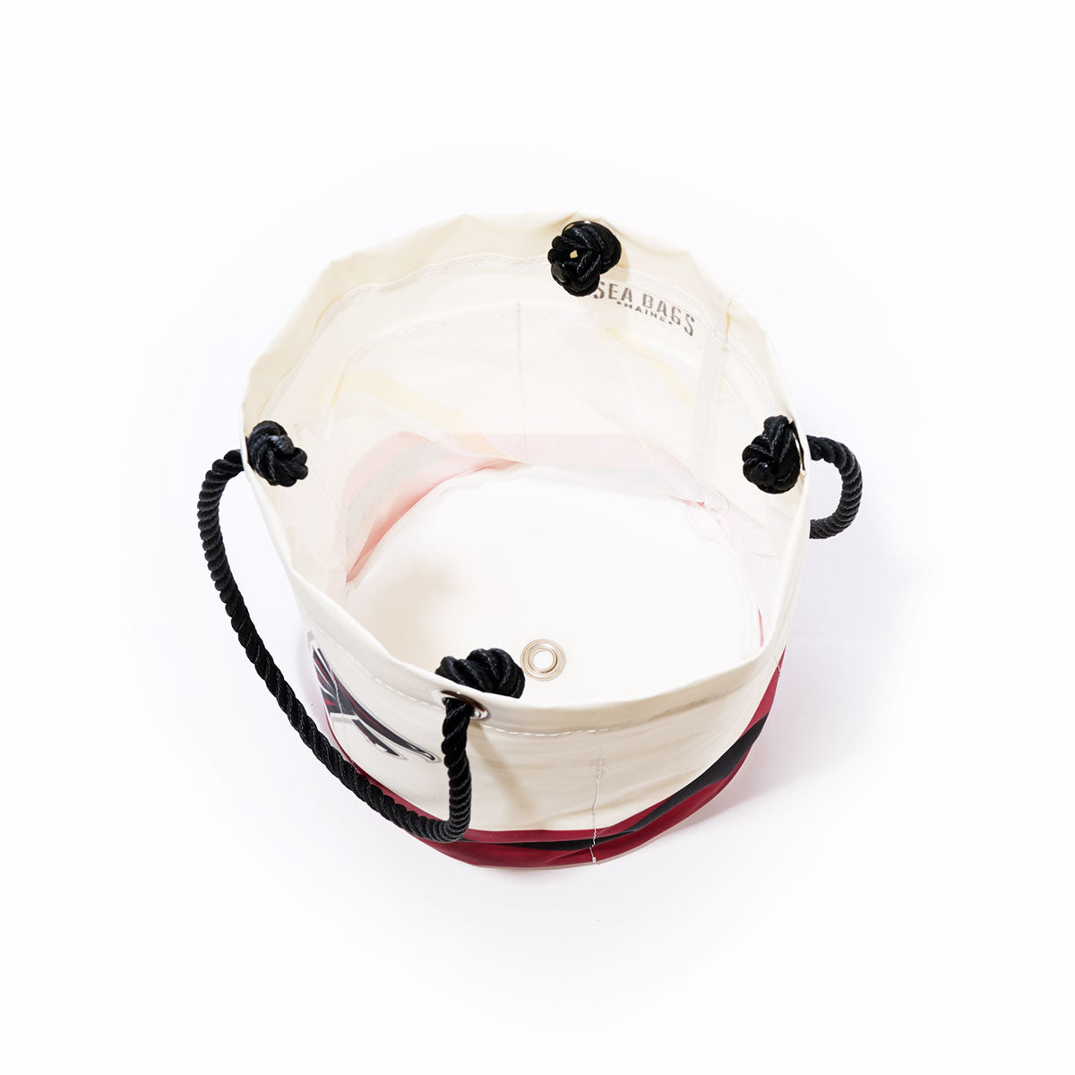 The Atlanta Falcons Beverage Bucket by Sea Bags is a round white and red bucket bag made from recycled sail cloth, featuring black rope handles secured with four black knots and a metal grommet at the base, as seen from above. by Sea Bags