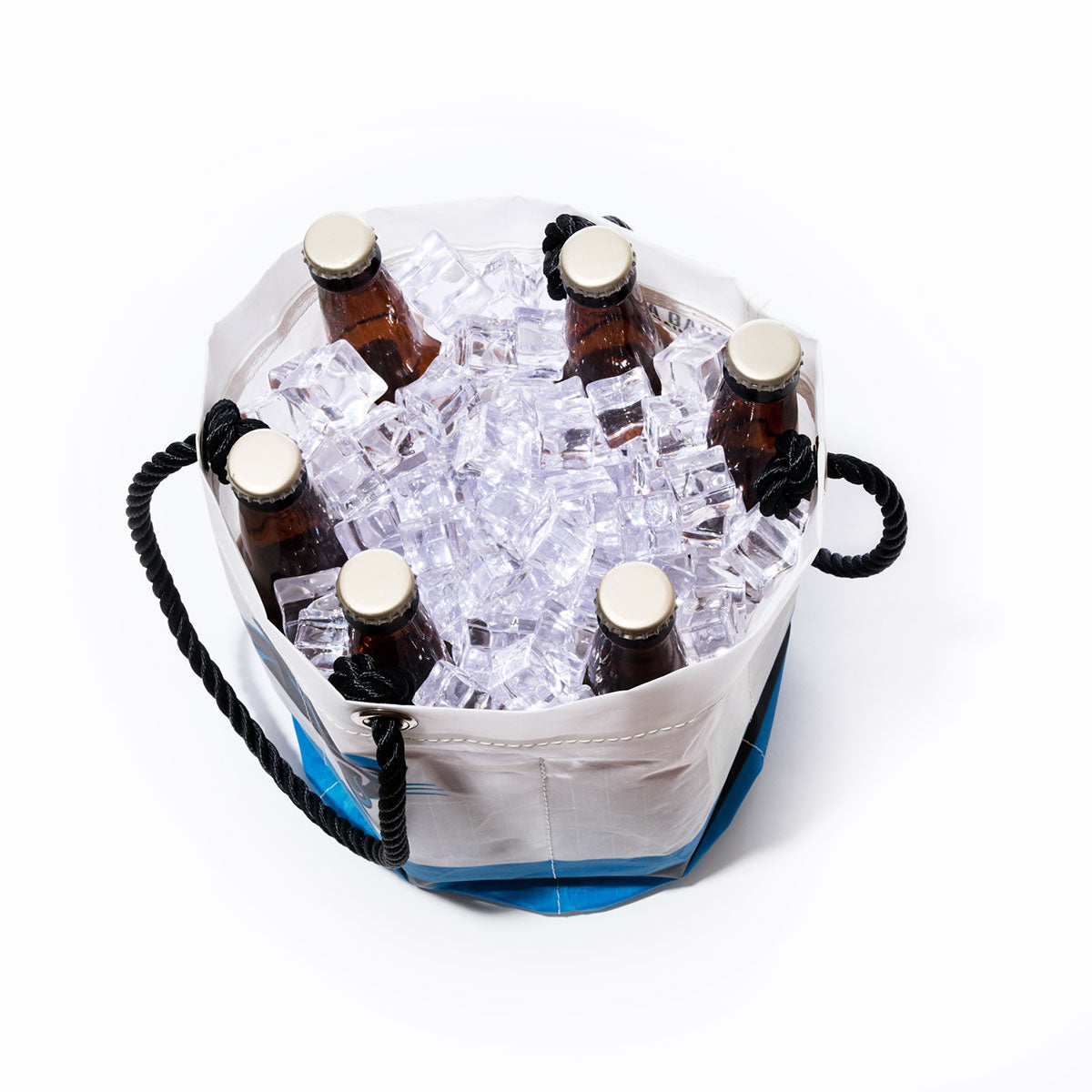 Six capped glass bottles are chilled in the Sea Bags Carolina Panthers Beverage Bucket, a sustainable cooler crafted from recycled sail cloth. They’re nestled among ice cubes in the white bucket and viewed from above against a plain white background. by Sea Bags