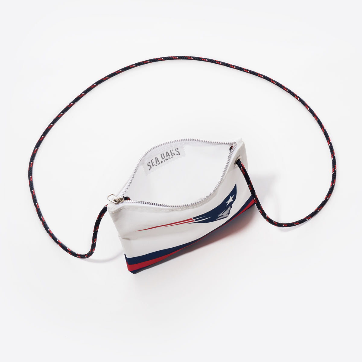 The Sea Bags New England Patriots Slim Crossbody is a small zippered pouch crafted from recycled sail cloth, featuring a navy blue, red, and white design with a stylized Patriots face logo. This sustainable crossbody bag includes a long, thin black strap arranged in a loop. by Sea Bags