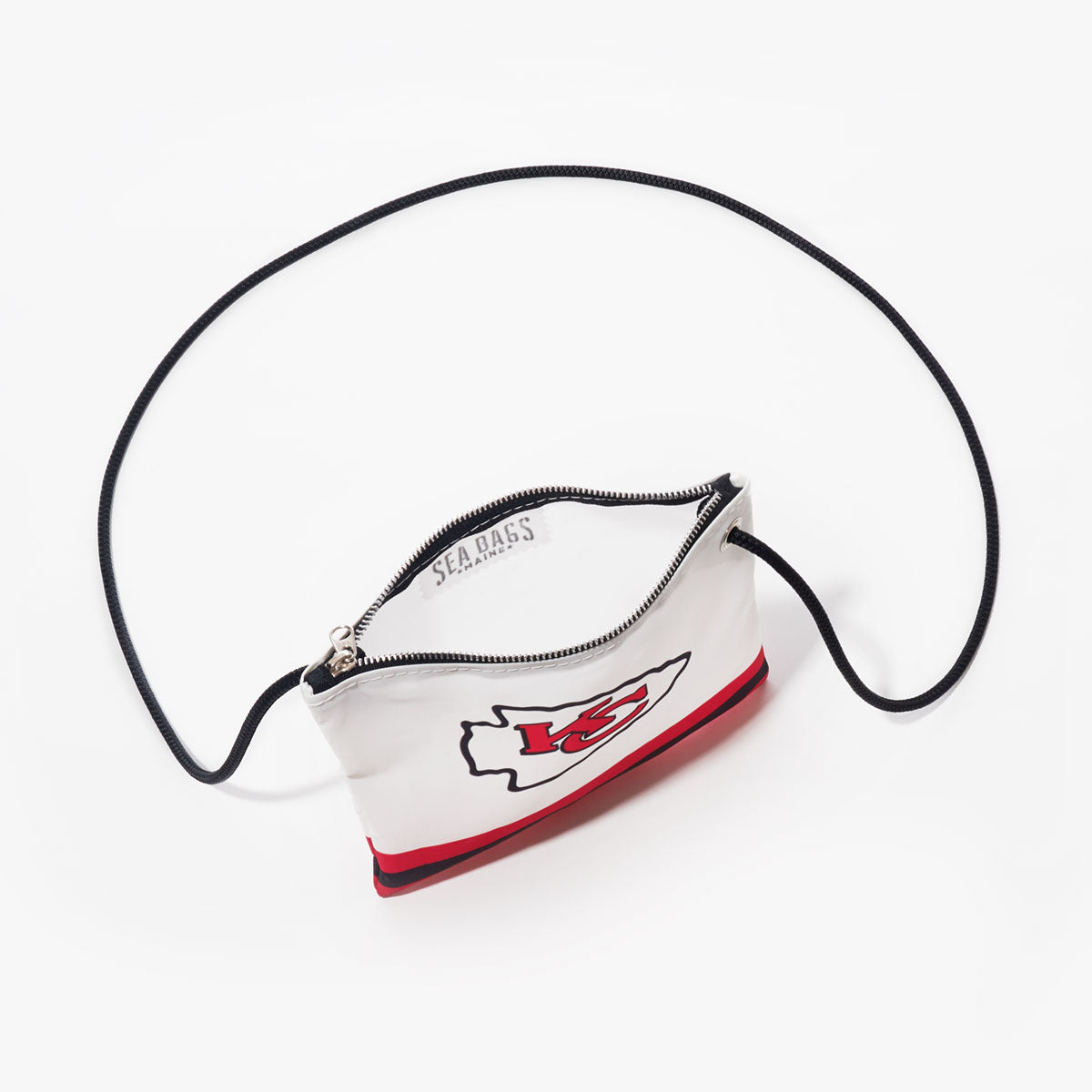 Introducing the Kansas City Chiefs Slim Crossbody by Sea Bags—a compact white crossbody bag designed with a bold red stripe at the bottom, sleek black zipper, and a slim black strap. Crafted sustainably, this accessory is photographed on a white background and proudly displays the iconic Chiefs logo, making it perfect for dedicated fans. by Sea Bags