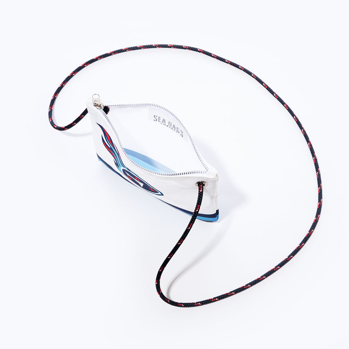 A white Sea Bags Tennessee Titans Slim Crossbody, made from recycled sail cloth, features a navy, red, and light blue logo graphic and a long, thin, patterned rope strap—this sustainable crossbody bag is set against a plain white background. by Sea Bags