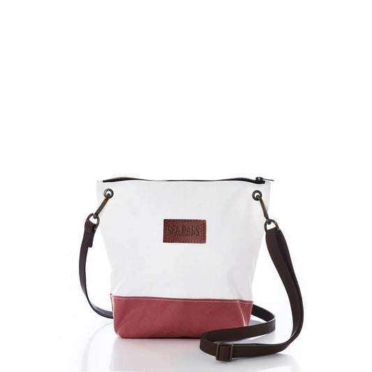 The Sea Bags Nantucket Red Chebeague Crossbody Bag features a two-tone design with a white upper made from recycled sail cloth and a Nantucket Red cotton canvas base. It is accented by a dark adjustable strap and a brown leather Sea Bags patch on the front, all displayed against a plain white background. by Sea Bags