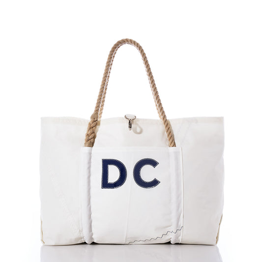 Sea Bags Custom Monogram Wharf Tote—crafted from rugged sail cloth, this white tote features sturdy rope handles, a convenient front pocket, and bold dark blue custom monogram letters on the front. Displayed against a white background, it’s the perfect personalized sail bag or classic Sea Bags tote. by Sea Bags