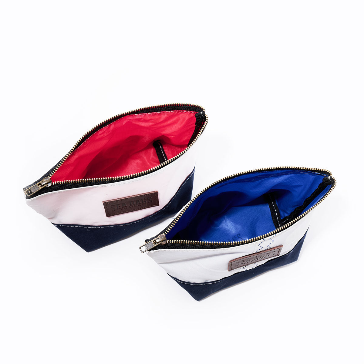 Two Chebeague Cosmetic Bags by Sea Bags are shown from above; one features a red interior and the other a blue interior. Both bags have white tops made from recycled sailcloth, sturdy dark canvas and leather bottoms, and leather side patches—making them ideal as stylish cosmetic bags or organizers. by Sea Bags