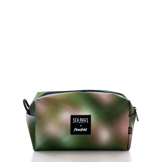 Introducing the Dragon Skin Toiletry Bag by Sea Bags—a rectangular bag featuring a green and brown camouflage design, sleek black zipper, and a prominent front label displaying Sea Bags x Flowfold. Crafted with sustainability in mind, this stylish and functional toiletry bag is the perfect companion for your next adventure. by Sea Bags