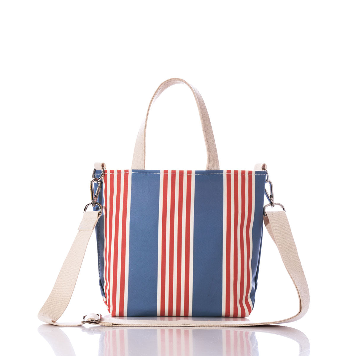 The French Stripe Crossbody Tote by Sea Bags is a small recycled sailcloth bag showcasing blue and red vertical stripes in a classic French stripe design. It features two short cream handles and a detachable cream shoulder strap, photographed on a white background. by Sea Bags