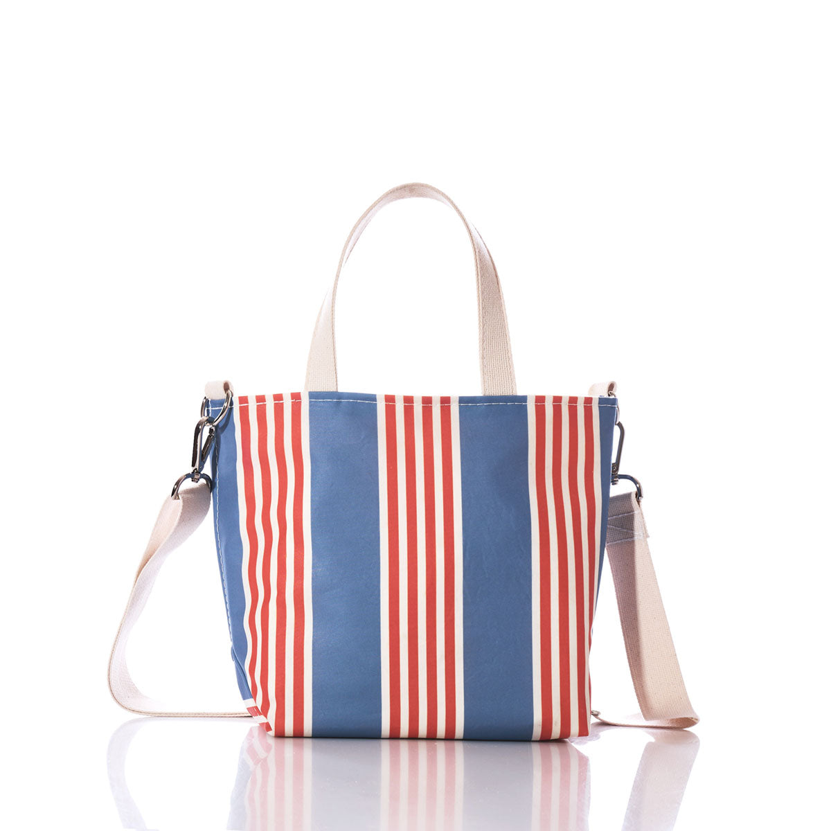 The Sea Bags French Stripe Crossbody Tote is a tote-crossbody hybrid crafted from recycled sailcloth, featuring blue and red vertical stripes, white handles, and an adjustable beige shoulder strap. It is displayed on a white background. by Sea Bags