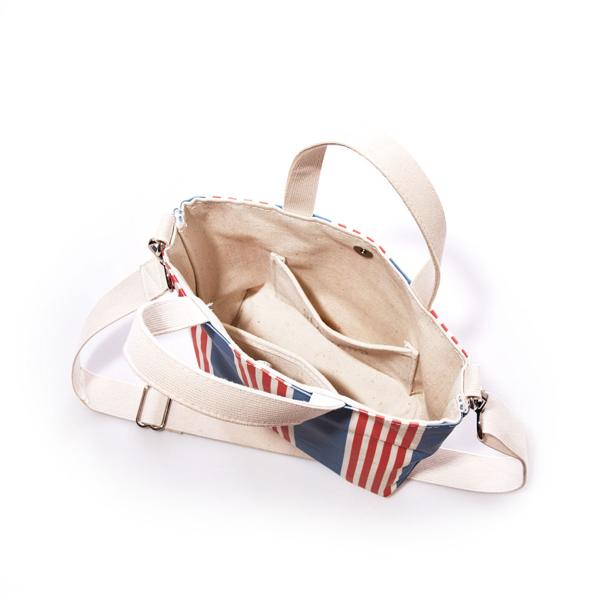The Sea Bags French Stripe Crossbody Tote is an open cream-colored canvas hybrid bag featuring a red and blue French stripe design on the exterior, two interior pockets, a zipper closure, and an adjustable shoulder strap, displayed against a white background. by Sea Bags