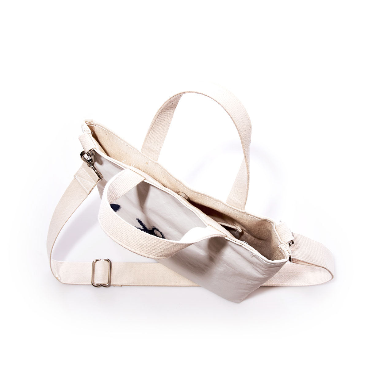 The Navy Anchor Crossbody Tote by Sea Bags, crafted from recycled sailcloth and featuring a zipper closure and two handles, is pictured from above on a white background to reveal its interior pocket. This eco-friendly bag blends practical design with sustainable style. by Sea Bags