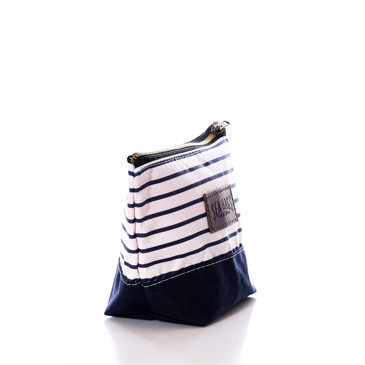 The Sea Bags Navy Mariner Stripe Chebeague Cosmetic Bag is a small zippered pouch, crafted from recycled sailcloth with navy and white horizontal stripes and a dark navy canvas and leather base, shown standing upright against a white background. by Sea Bags