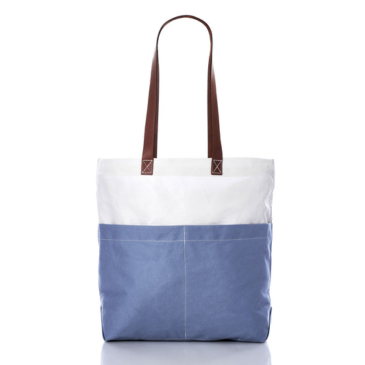 The Chambray Blue Chebeague Market Tote by Sea Bags, crafted from recycled sails, showcases a two-tone design with a blue bottom and white top, functional front pockets, and sophisticated brown leather handles, all set against a white background. by Sea Bags