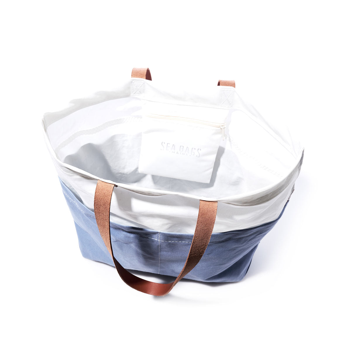 The Sea Bags Chambray Blue Chebeague Market Tote is a large bag crafted from recycled sails, featuring sturdy brown leather handles, a white upper section, blue lower section, and an attached white pouch inside. by Sea Bags