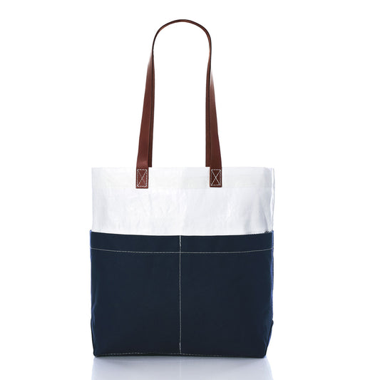 The Sea Bags Navy Chebeague Market Tote, crafted from recycled sails, features a white upper section, navy blue lower section, front pockets, and brown leather handles. It is presented against a white background. by Sea Bags