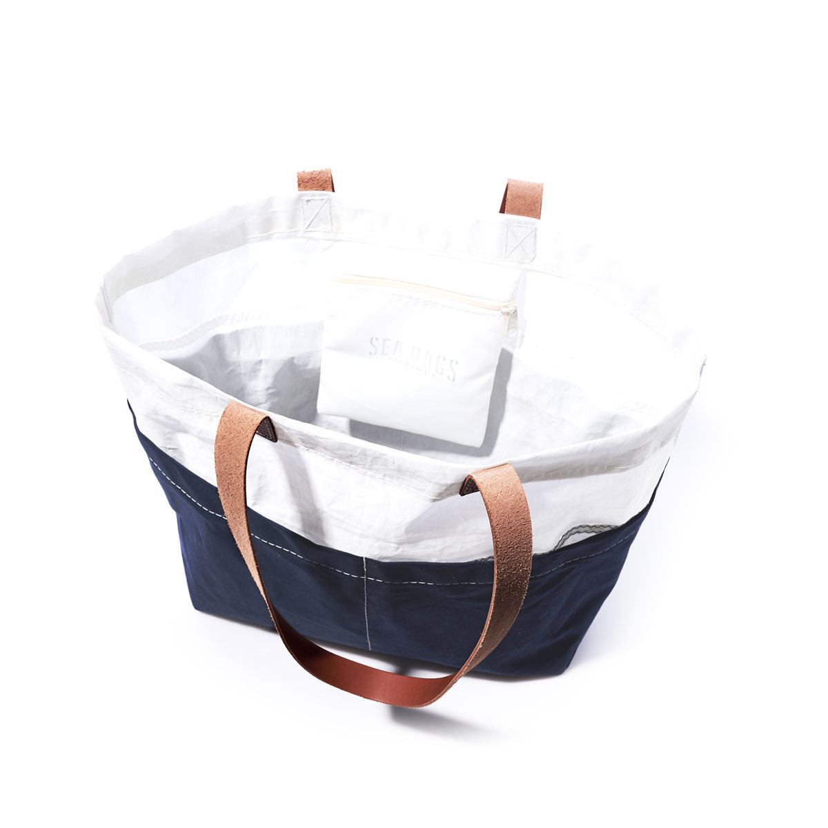The Navy Chebeague Market Tote by Sea Bags is crafted from recycled sails and features sturdy brown leather handles along with a small white pouch inside. by Sea Bags