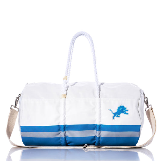 The Sea Bags Detroit Lions Duffel features white and blue sail cloth, rope handles, a tan shoulder strap, and a bold blue lion logo on the side—an eye-catching NFL accessory for devoted Detroit Lions fans, shown on a white background. by Sea Bags