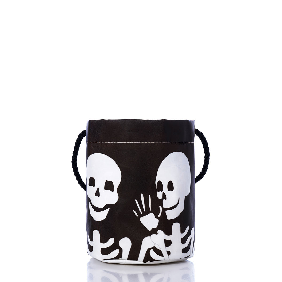 Introducing the Sea Bags “Bucket of Bones Bag”—an eco-friendly Halloween candy bucket crafted from recycled sail material, featuring two white skeletons on a black bucket with rope handles, one appearing to whisper to the other.