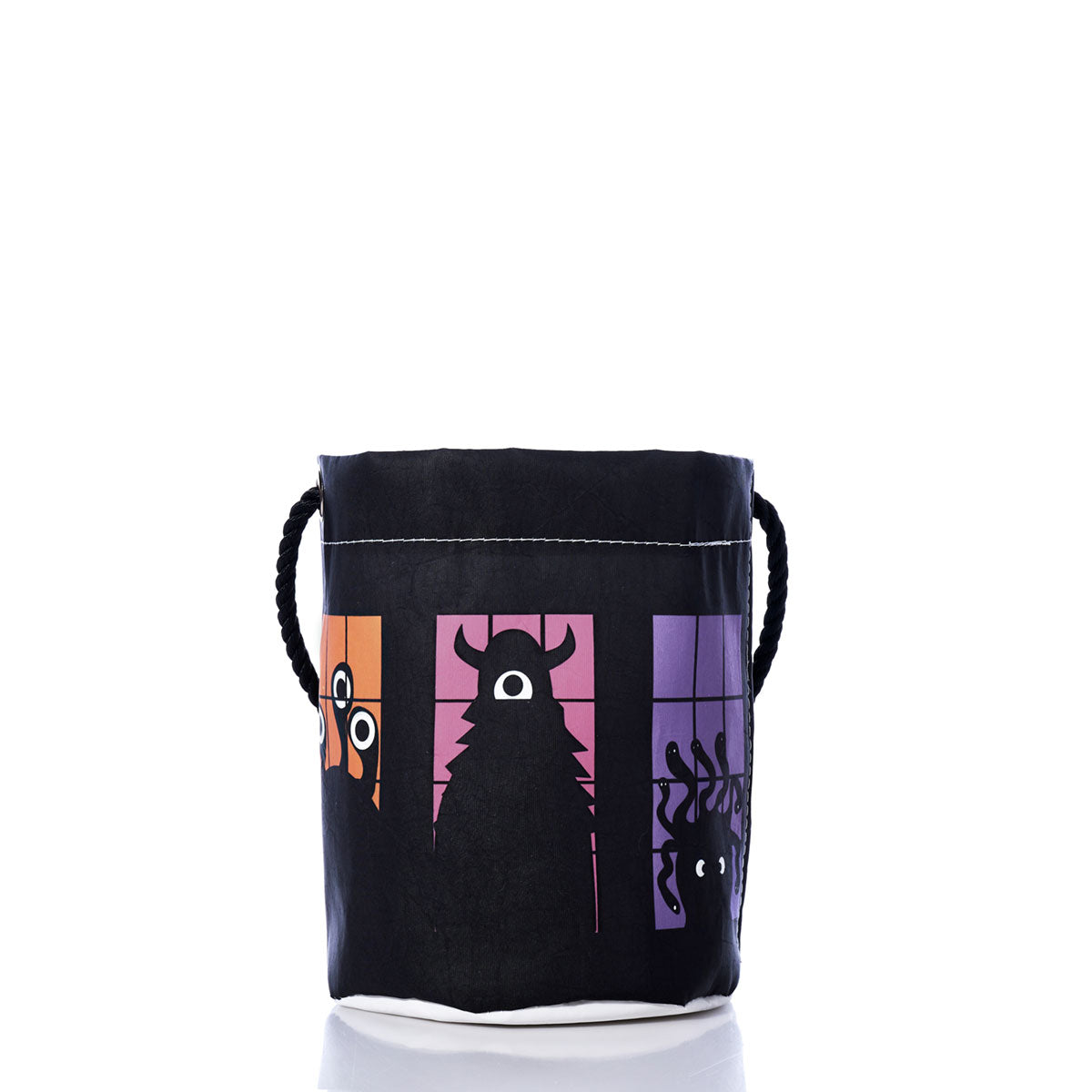 Sea Bags’ Monster Party Bucket Bag is an eco-friendly Halloween or monster party accessory made from recycled sails, featuring black fabric with rope handles and playful cartoon monster silhouettes in orange, pink, and purple panels on a white background.