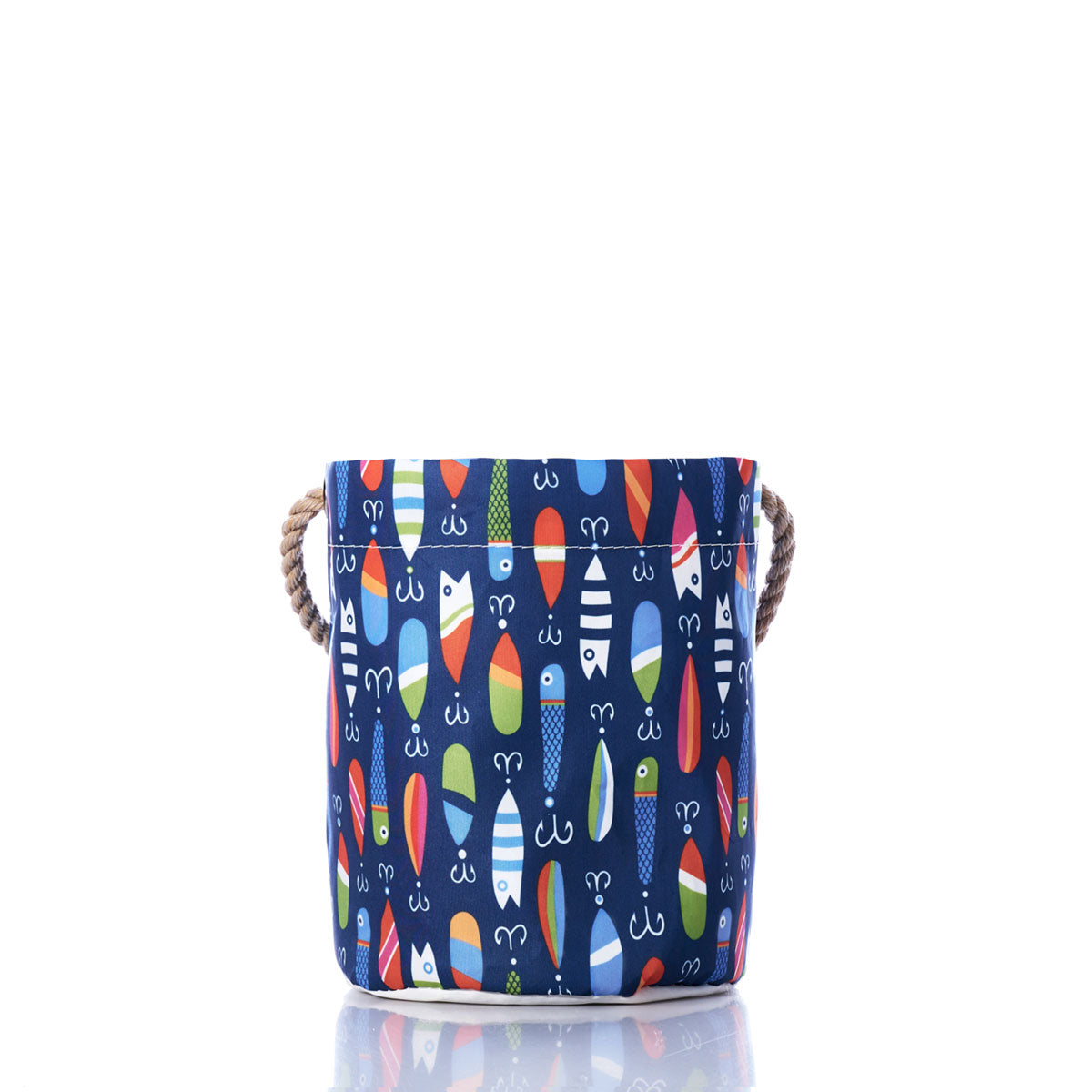 The Kate Nelligan Lures Bucket Bag by Sea Bags features a blue fabric design with a multicolored surfboard pattern, sturdy rope handles on each side, and coastal prints that evoke a nautical feel, all set against a crisp white background. by Sea Bags
