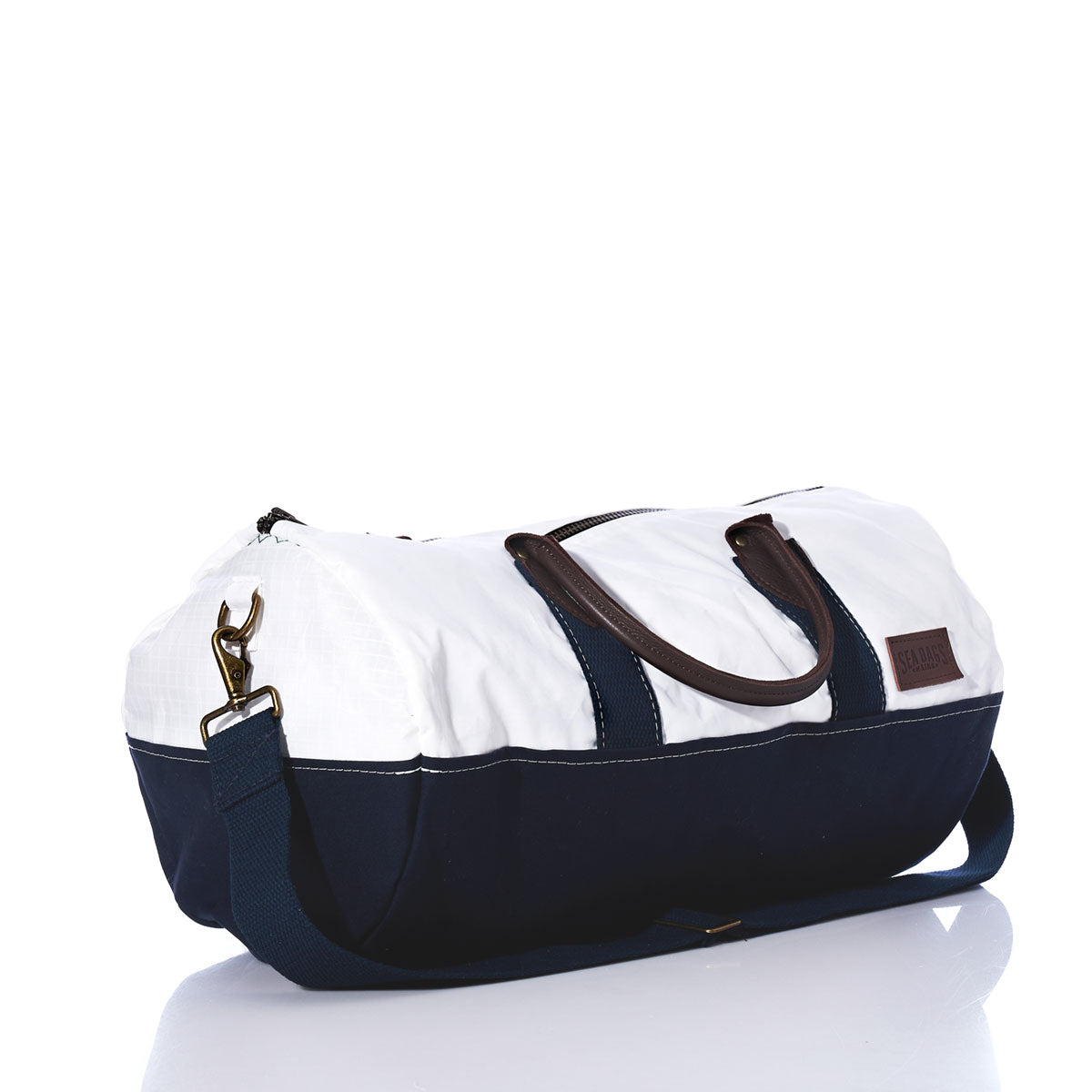 The Chebeague Duffel by Sea Bags is crafted from recycled sail in white and navy blue fabric, featuring premium leather handles, a detachable navy shoulder strap, and a brown patch on the side, shown on a white background. by Sea Bags