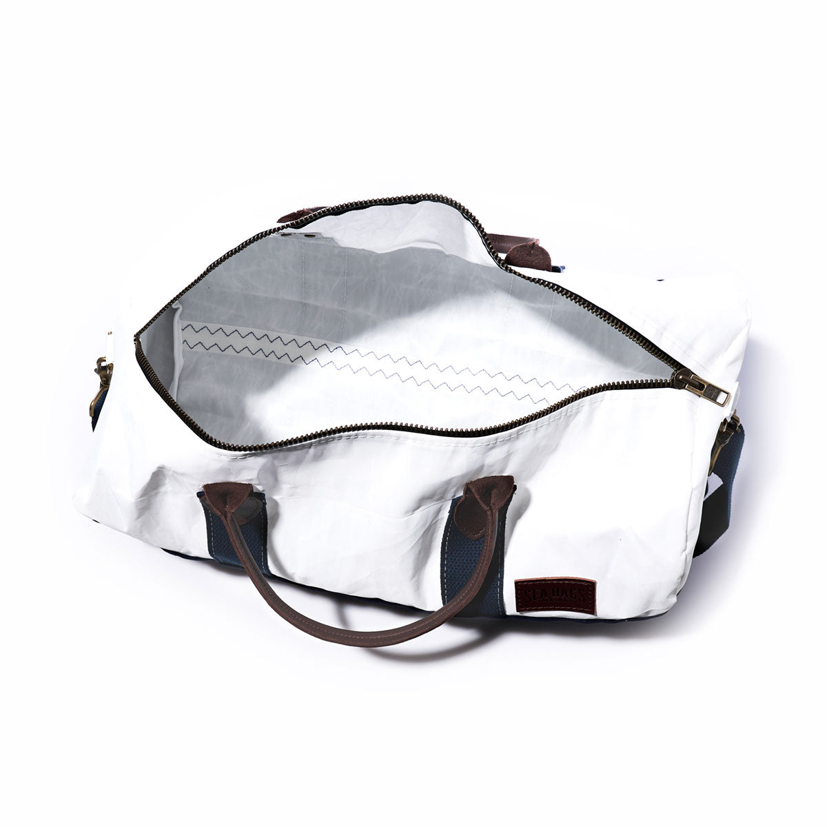 The Sea Bags Custom Chebeague Duffel features a stylish white design with brown leather handles, navy blue straps, and an open zipper that reveals a spacious, empty interior lined in grey—making this versatile carry-on bag perfect for travel or everyday use. by Sea Bags