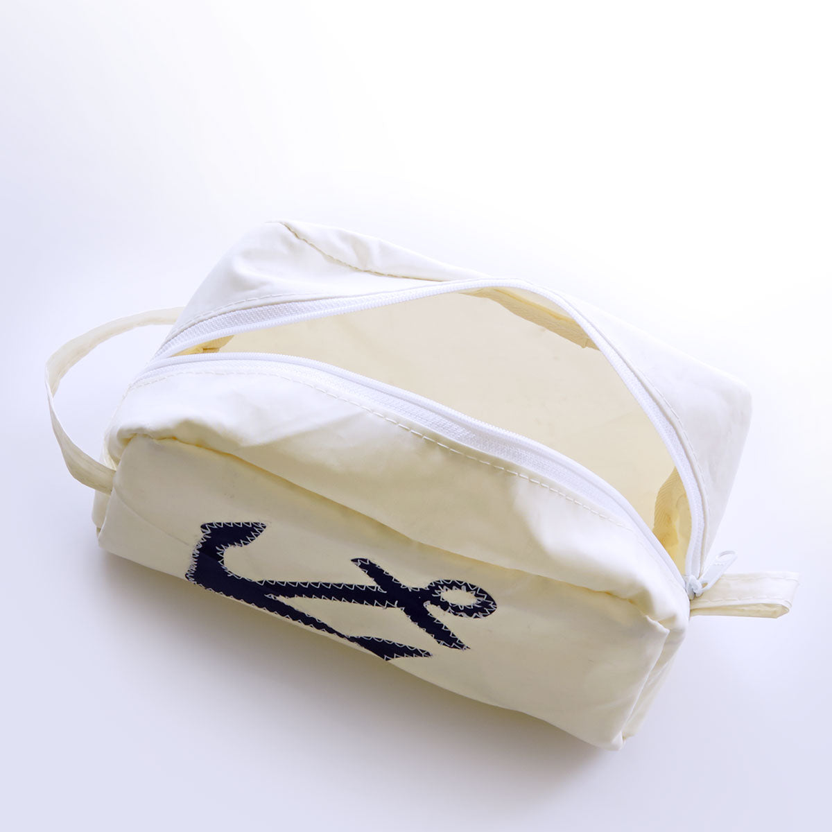 The Navy Anchor Toiletry Bag by Sea Bags, crafted from recycled sail material, features a classic white design with a blue anchor motif and a zippered closure. The bag is partially open to display its light-colored interior and is photographed on a white background. by Sea Bags