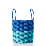 The Fisherman Rope Basket - Blue  Teal by Custom Cordage / DBA Maine Rope Mats is a round, handcrafted basket with two handles, made in Maine from eco-friendly materials. It features thick blue and teal braided rope arranged in a horizontal pattern and is shown on a white background. by Sea Bags