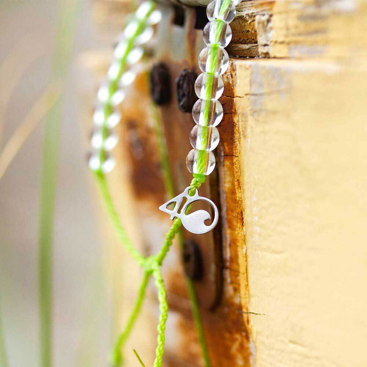 Two 4ocean Beaded Bracelets - Sea Turtle by 4ocean, featuring lime green cords, clear beads, and a silver circular logo charm, inspired by ocean conservation and sustainable jewelry, hang against a weathered yellow wooden surface. by Sea Bags