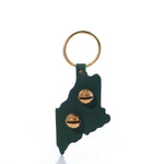 Introducing the State of Maine Door Chime by true—a green, Maine-shaped keychain inspired by classic New England Bells. It features two gold pins and a gold key ring at the top, evoking the charm of a traditional Maine door chime.