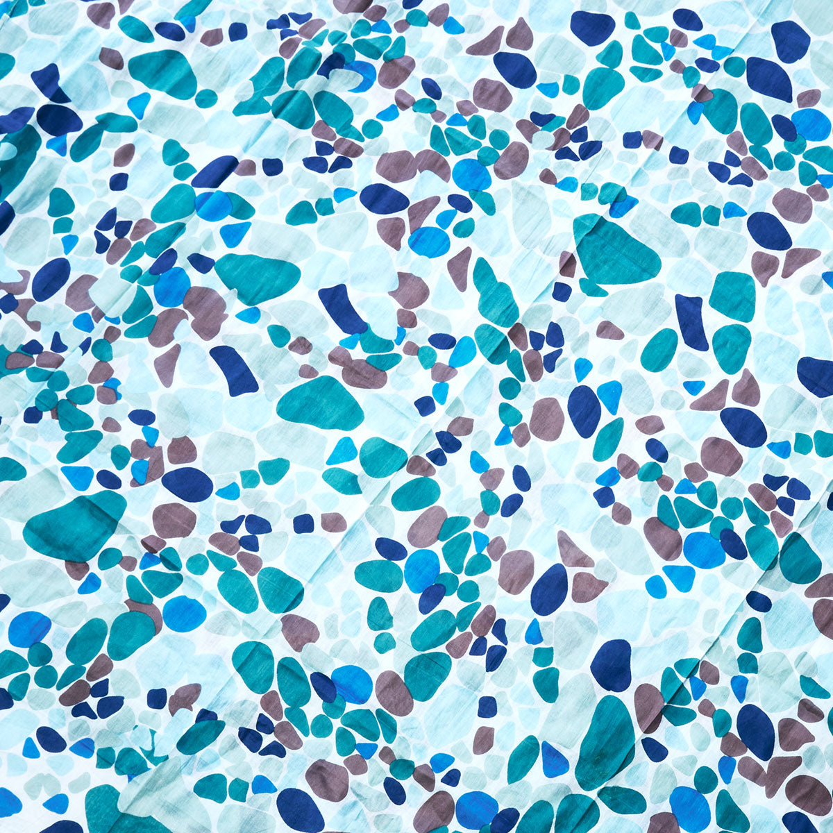 The Sea Glass Scarf by Batela USA Inc features an abstract pattern of scattered blue, teal, and brown shapes on a white background, reminiscent of sea glass pebbles gently smoothed by the ocean for a nautical-inspired charm. by Sea Bags