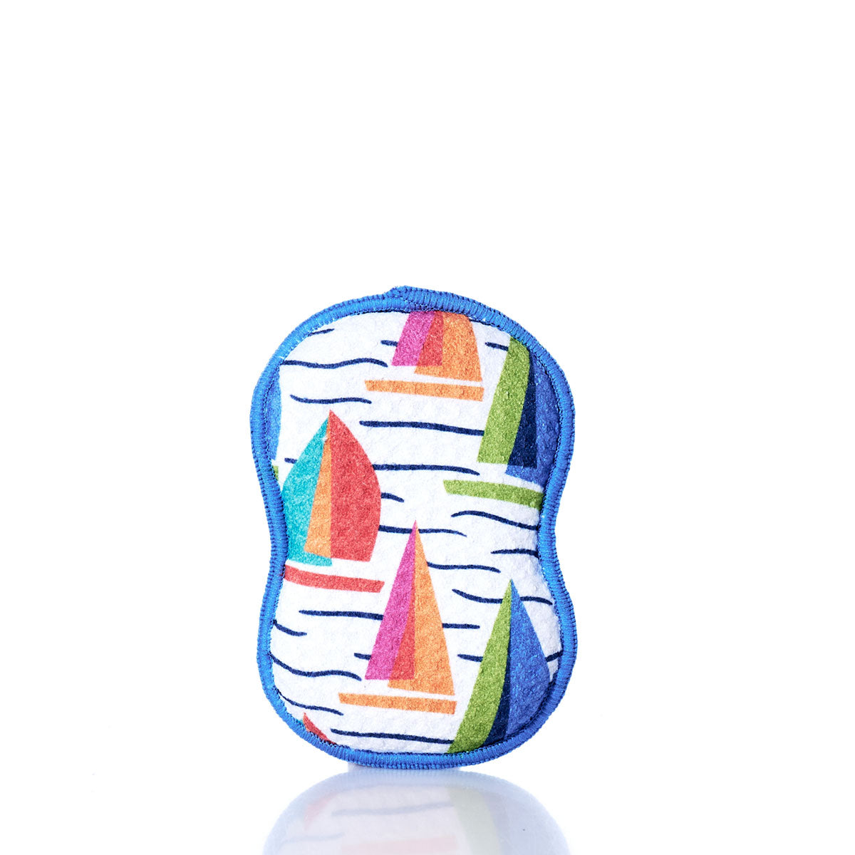 The Kate Nelligan Full Sail Dish Sponge by Once Again Home is a colorful, reusable sponge with blue trim and a cheerful sailboat pattern, crafted from recycled materials. It stands upright on a white reflective surface against a plain white background—an ideal addition to your sustainable home textiles collection. by Sea Bags