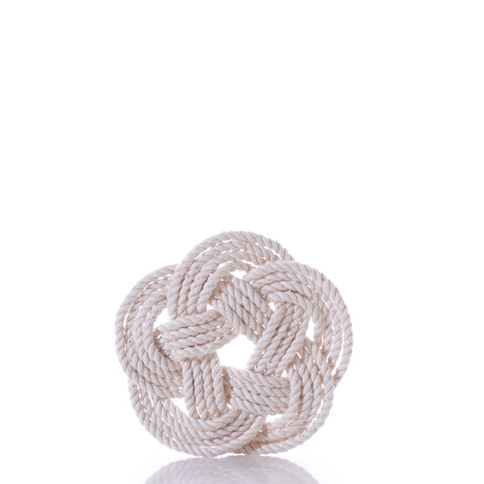 A natural-colored rope is tied in a decorative, circular Turk’s head knot—reminiscent of Nautical Sailor Knot Coasters-Natural from Mystic Knotwork—and placed on a white background with a faint reflection below it.