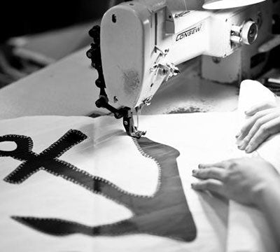 Black-and-white close-up of a sewing machine stitching an anchor emblem onto sailcloth