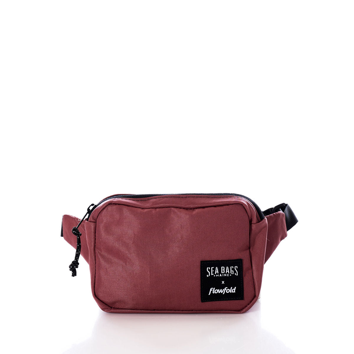 A Vintage Tanbark Crew Belt Bag by Sea Bags, crafted from recycled sail cloth in maroon with a black zipper, adjustable strap, and a black patch labeled Sea Bags x Flowfold on the front. Displayed against a white background, this sustainably made accessory blends eco-conscious design with style. by Sea Bags